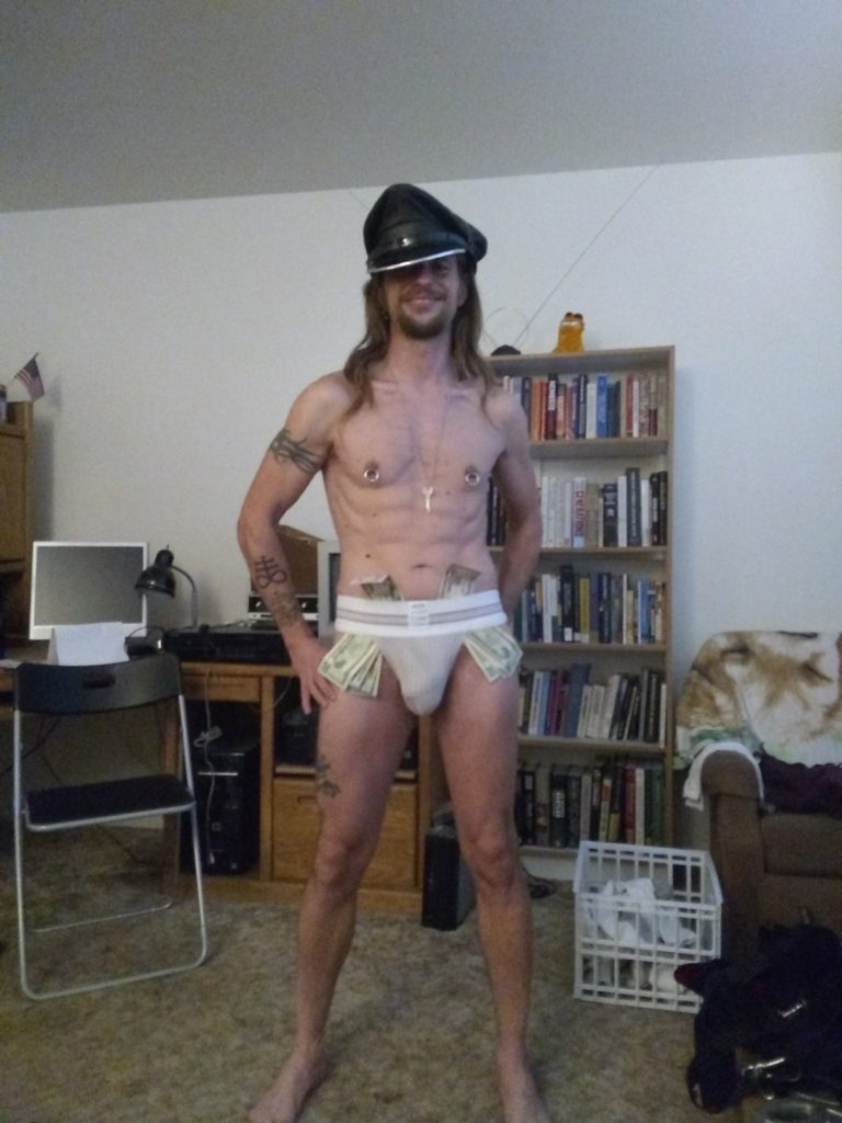 Jack Drago poses in his living room in Pacifica CA in nothing but a black leather muir cap, his chastity slave's keys, a jockstrap and $260