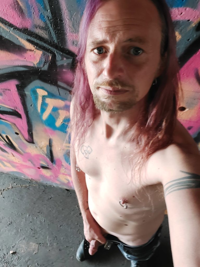 Purple haired punk with pierced nipples cruising under a bridge in Oakland CA