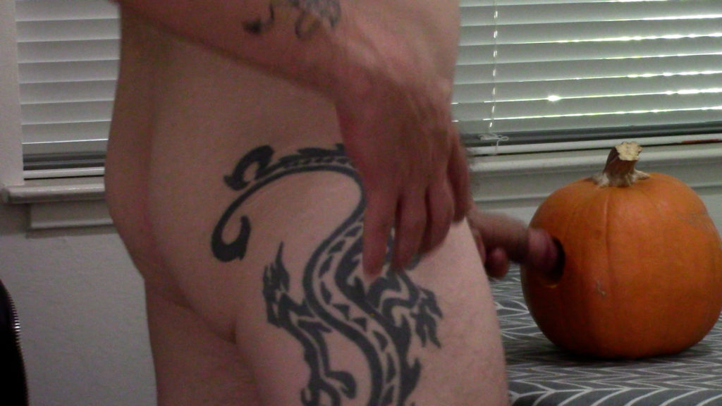 Tattooed man prepared to penetrate the pumpkin with his penis