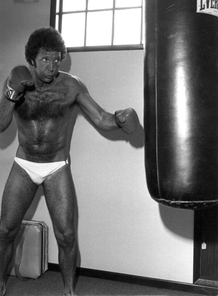 black and white image of Tom Jones in a posing strap beating an Everlast brand punching bag in the mid 70s.