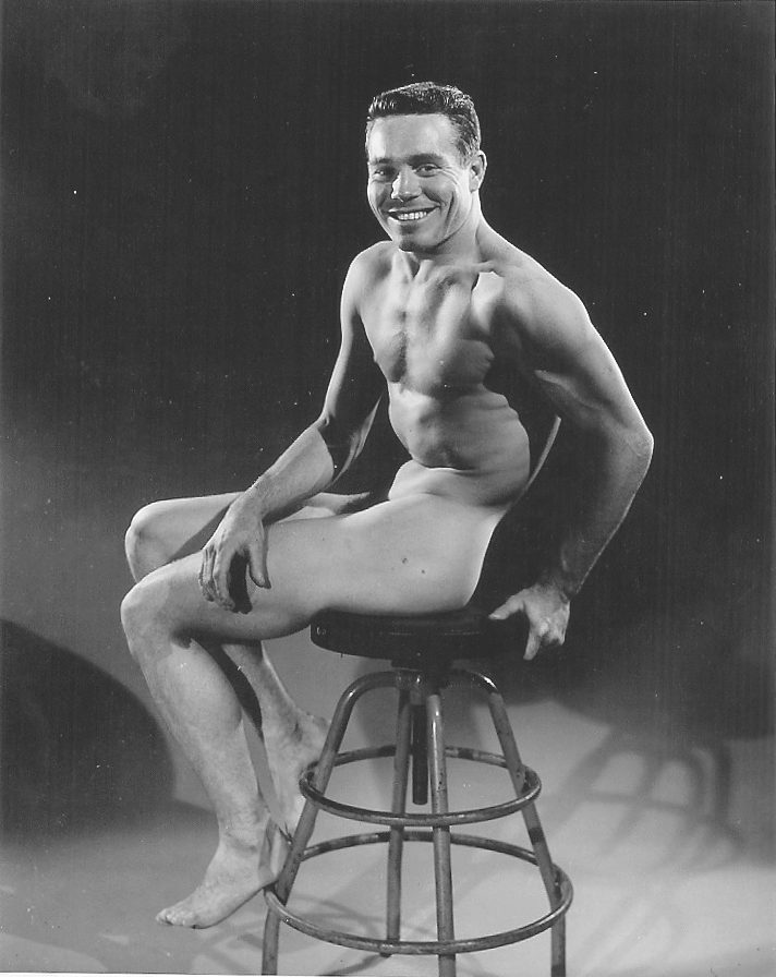 Jack LaLanne photographed nude in black and white by Bob Mizer, sitting on a 1940s style office stool.